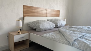 A modern bedroom with a wooden headboard, two bedside tables with lamps, and a bed with patterned bedding. - Modern apartment - top location (Witten)
