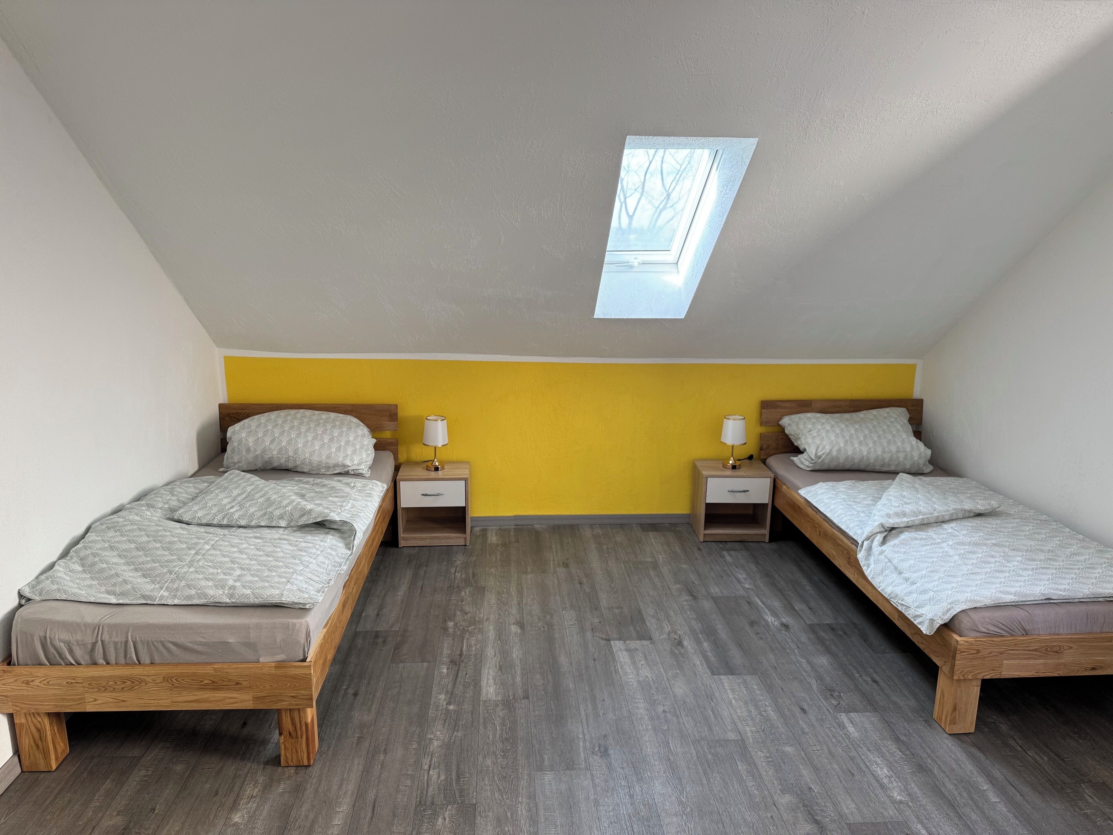 Ein Schlafzimmer mit zwei Betten, einem Oberlicht und einer gelben Akzentwand.