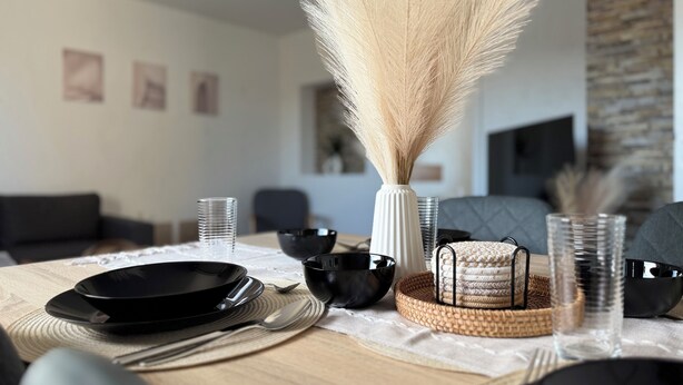 A dining table set with black plates, silverware, and clear glasses, with a vase of pampas grass and a woven basket centerpiece. - Modern apartment - top location (Witten)