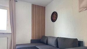 A modern living room with a grey sofa, a wooden slat wall, a round wall clock, and a window with curtains. - Modern apartment - top location (Witten)