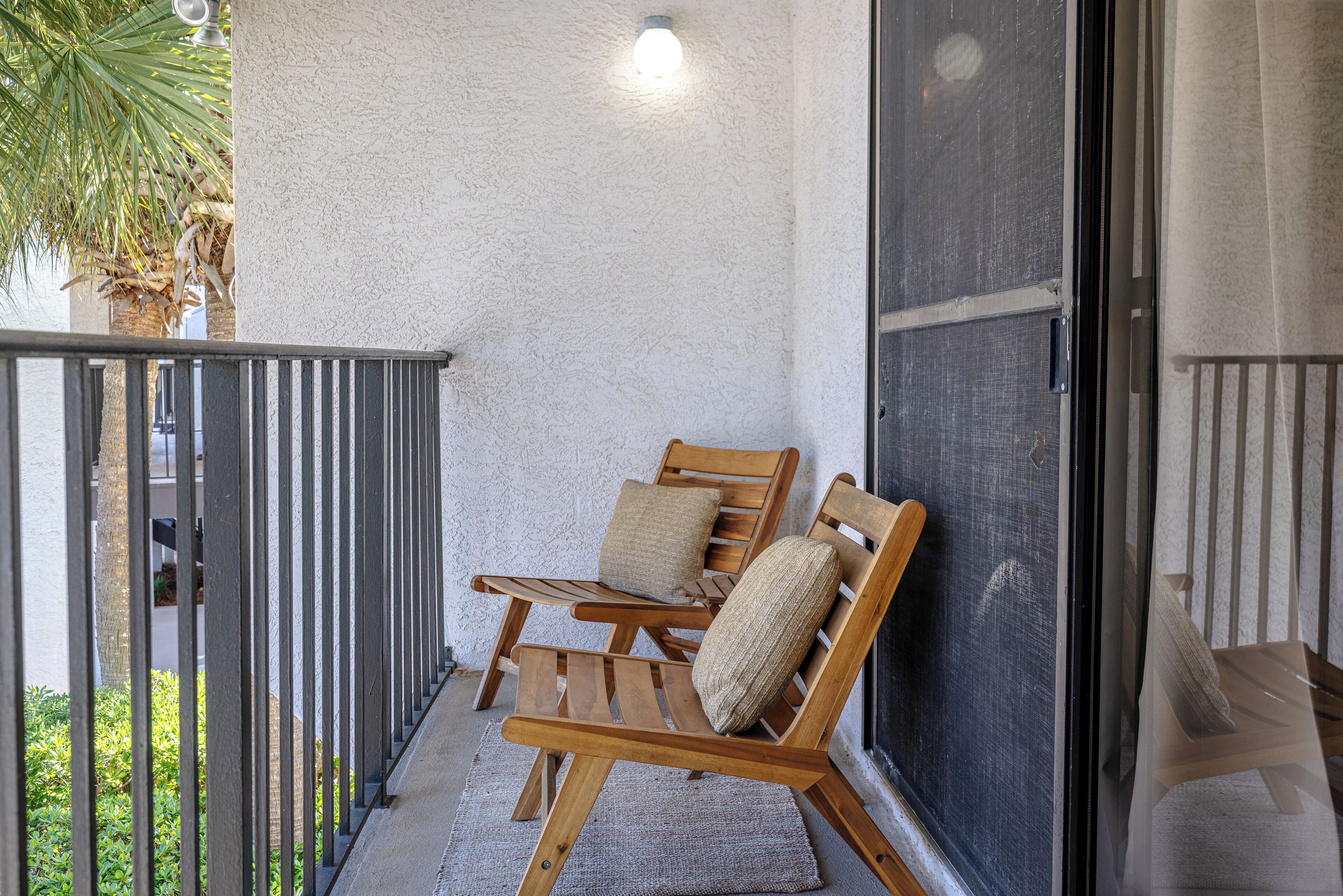 A balcony with two wooden chairs, a textured wall, and a view of greenery.