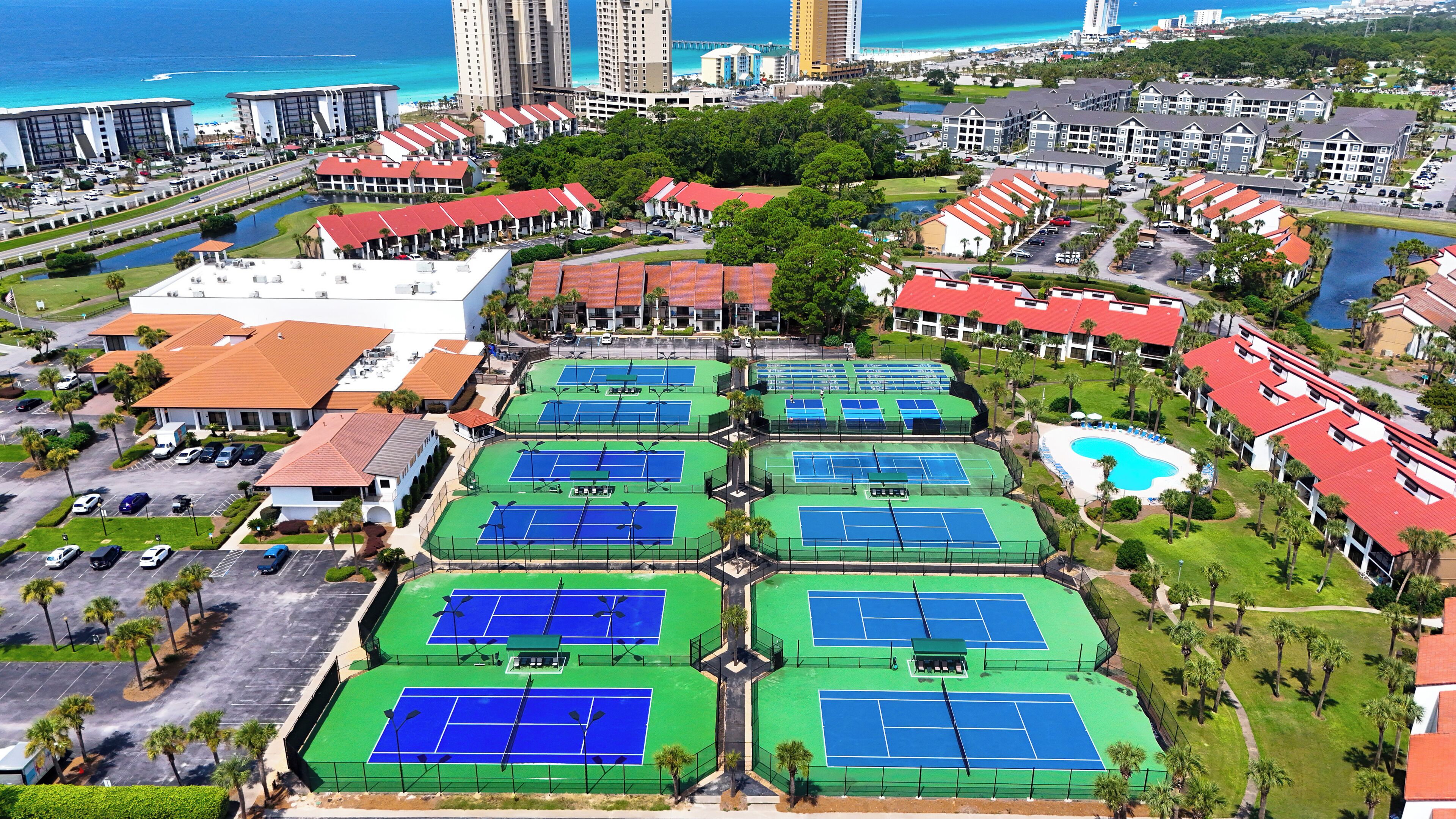A resort with multiple tennis courts, a swimming pool, and a view of the ocean.
