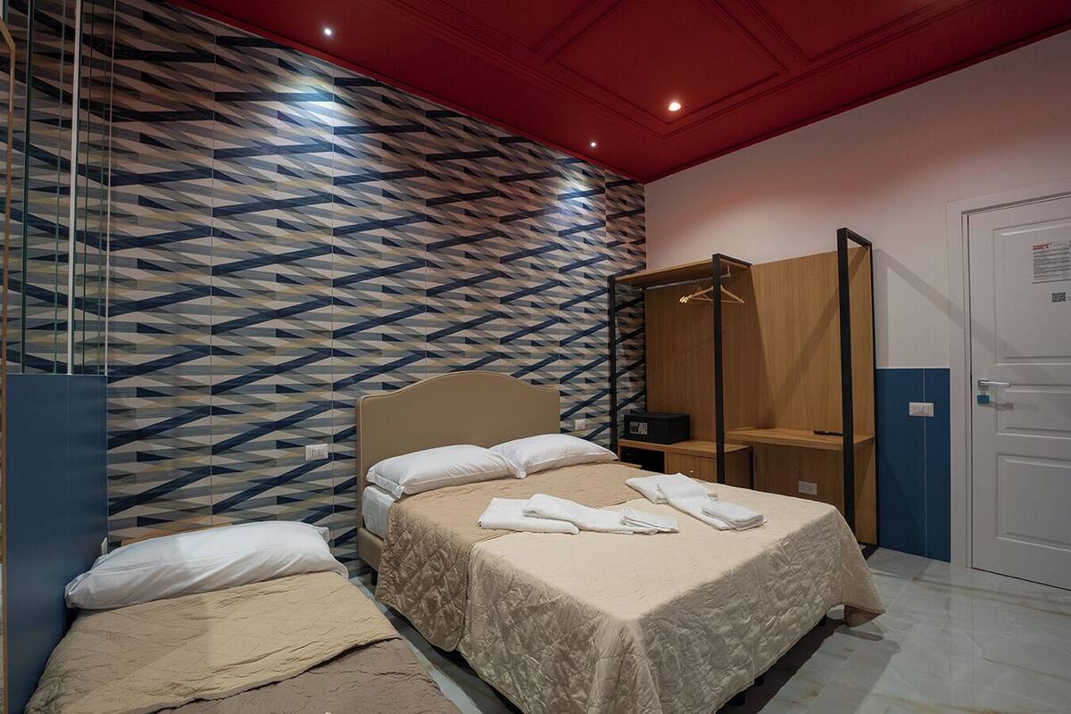 A hotel room with a bed, a mirror, a wardrobe, and a patterned wall.