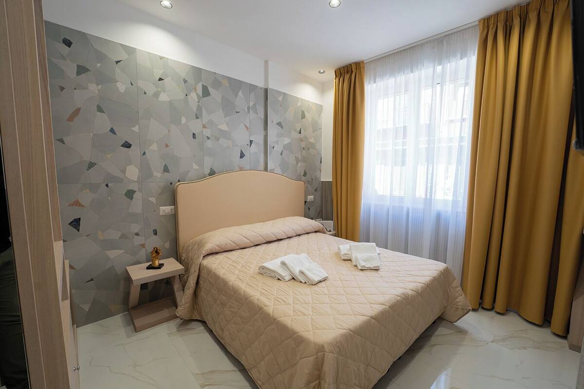 A hotel room with a bed, a nightstand, a decorative item, and a window with curtains.
