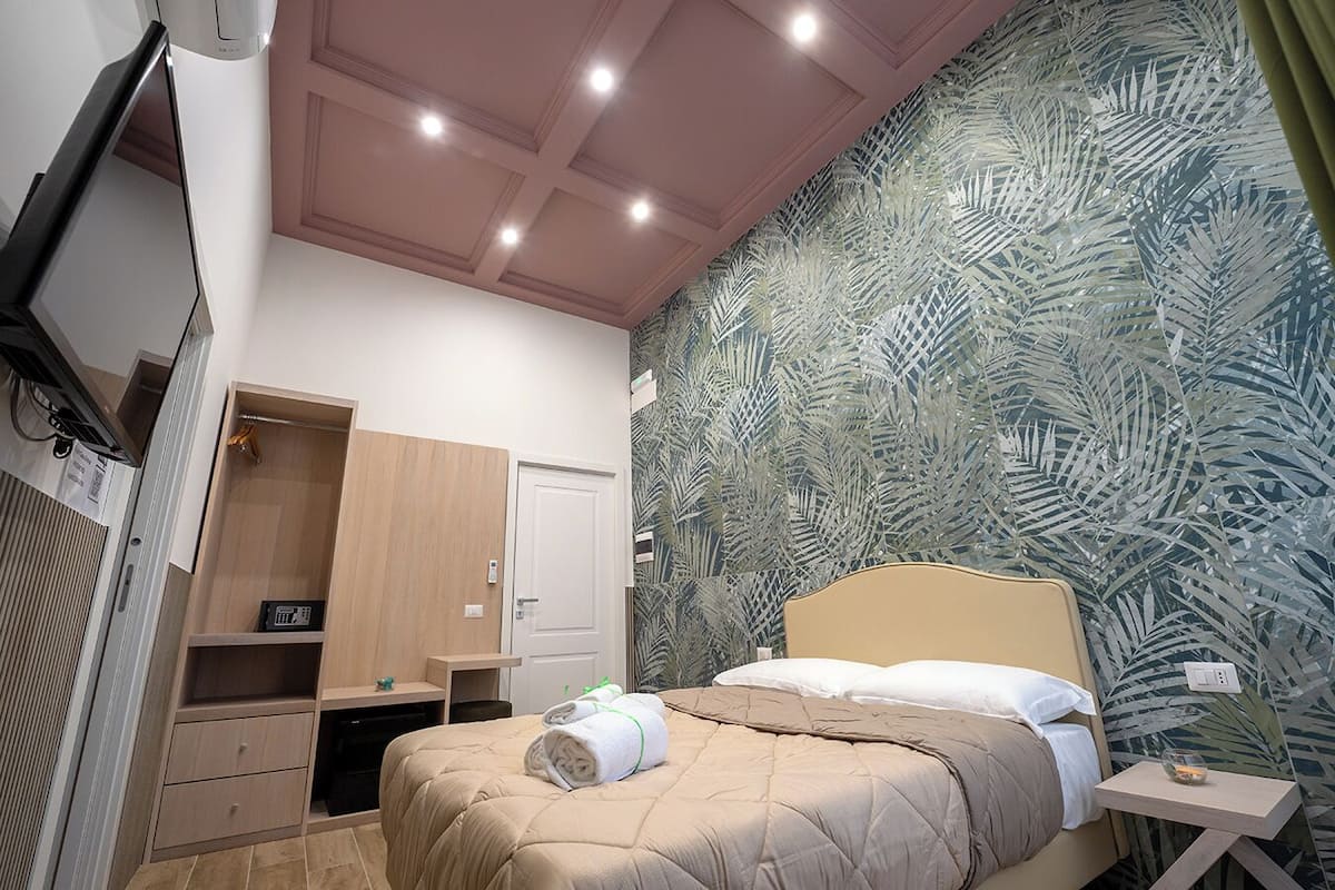 A bedroom with a bed, a wooden wardrobe, a desk, and a television.