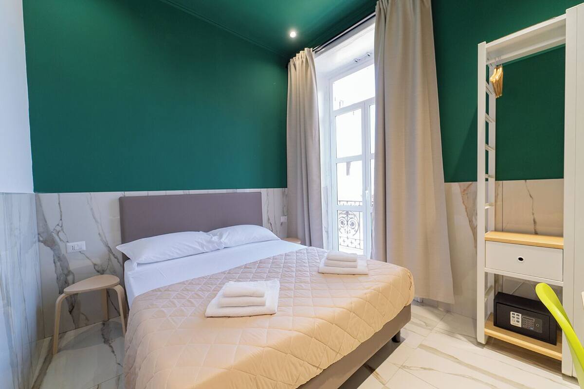 A bedroom with a bed, a nightstand, a wardrobe, and a window with curtains.