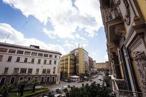 Straßenansicht mit Gebäuden, darunter ein gelbes Mehrstöckiges und ein weißes Gebäude mit Balkonen.