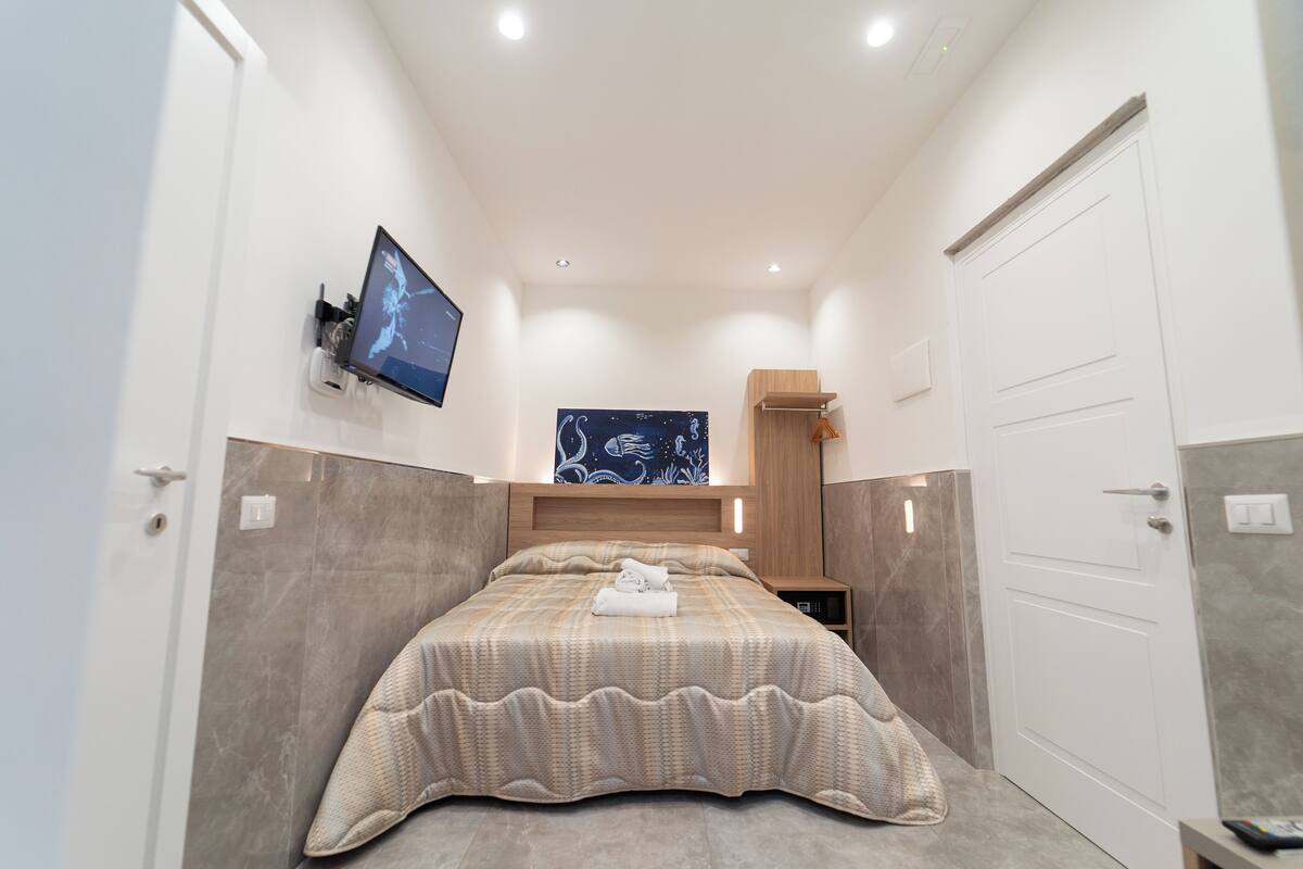 A modern hotel room with a large bed, a flat-screen TV mounted on the wall, and a wooden headboard.