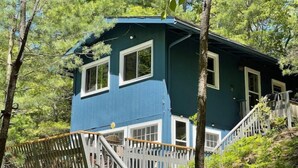 Una casa a due piani con facciata blu e finiture bianche, immersa nel verde.