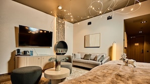 A modern hotel room with a large bed, a sofa, a TV, a round mirror, and a decorative ceiling light. - Balder Luxury Lodge & Glass Igloos (Kittila)