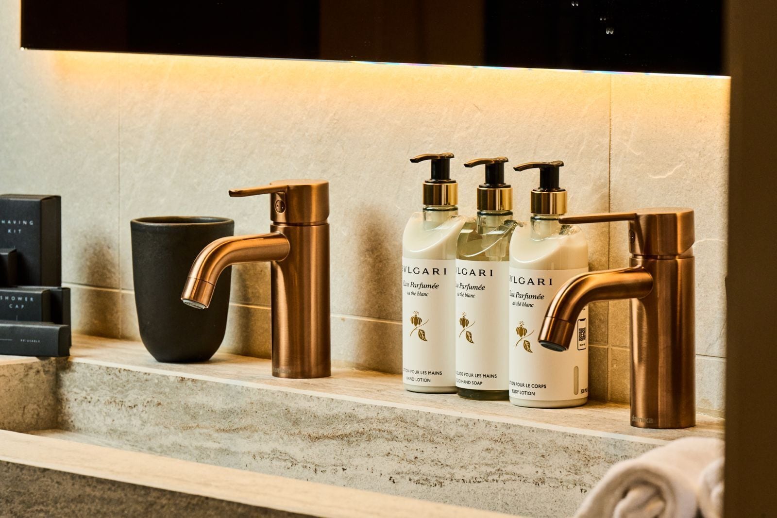 A bathroom vanity with a copper faucet, a black vase, and three bottles of Bulgari body lotion.