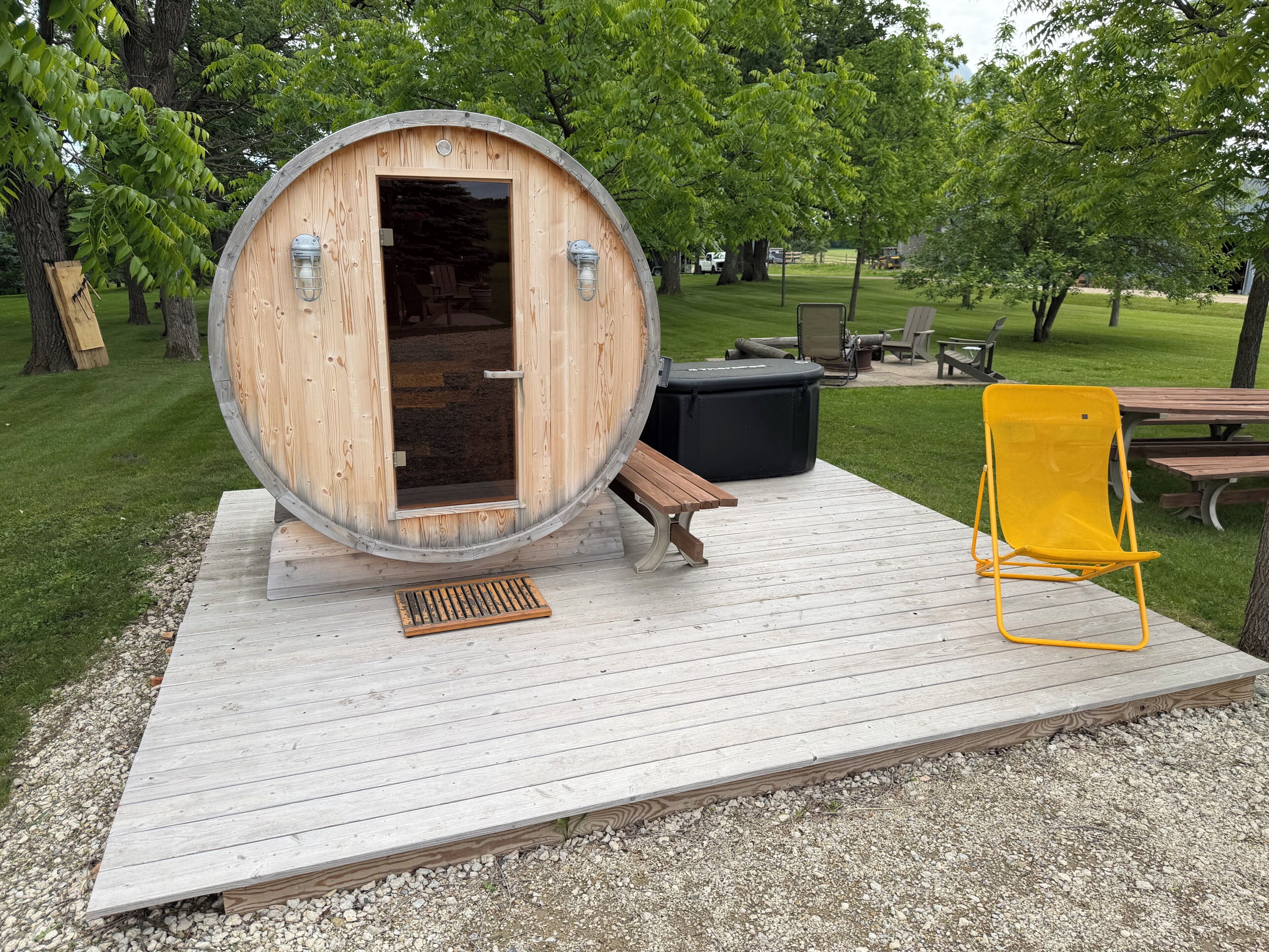 A wooden barrel structure with a bench and a yellow chair on a wooden deck.