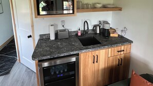 A compact kitchen with wooden cabinets, a built-in oven, a sink, and a coffee maker. - Alpaca Cabin #1 (Audubon)