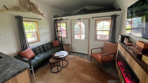 A cozy living room with a green sofa, a wooden coffee table, a leather armchair, and a fireplace. - Alpaca Cabin #1 (Audubon)
