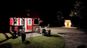 Una cabaña con porche, mobiliario exterior e interior bien iluminado.
