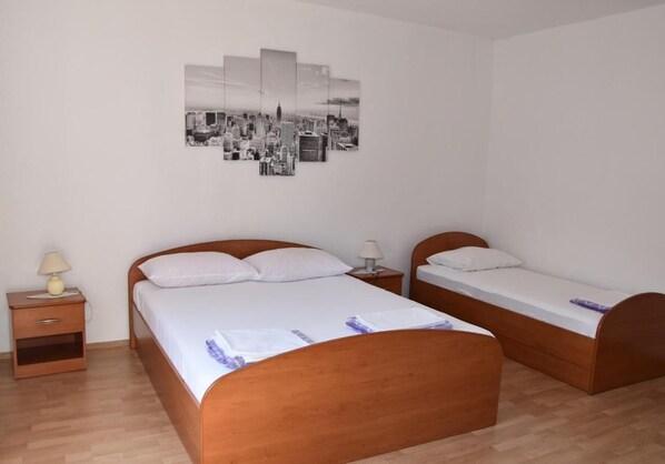 Hotellihuone, jossa on kaksi puista sänkyä, yöpöytä lampun kanssa ja seinällä kaupunkimaisemaa esittävä taideteos.