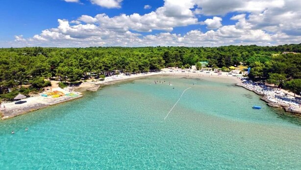 An aerial view of a beach with clear turquoise water, a sandy shore, and a forested hill in the background. - Charming 2-bedroom apartment with AC, WiFi in lovely Pakoštane (Pakoštane)