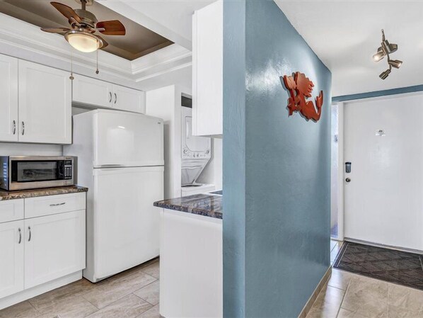 A kitchen with white cabinets, a microwave, a refrigerator, and a ceiling fan. - Riviera Club 204 | Oceanfront Views, Balcony + Beach Access (Fort Myers Beach)