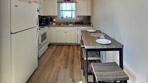 Une cuisine compacte avec des meubles blancs, un four encastré, un réfrigérateur et une table à manger avec des bancs.
