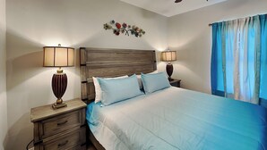 Une chambre à coucher avec un grand lit, deux tables de chevet avec des lampes, une tête de lit en bois et un motif floral décorant le mur.