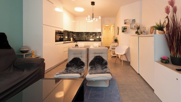 A modern living room with a sofa, a glass coffee table, and a dining area with a white chair. - Newly-built Apartment by the sea (Middelkerke)