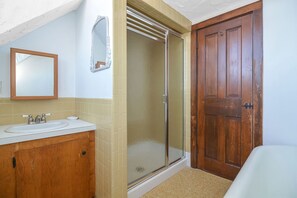 Een badkamer met een houten wastafelmeubel, een witte wastafel, een spiegel, een douchecabine met glazen wanden en een houten deur.