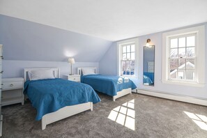 Een slaapkamer met twee bedden, een nachtkastje met een lamp, een dressoir en een groot raam met uitzicht.
