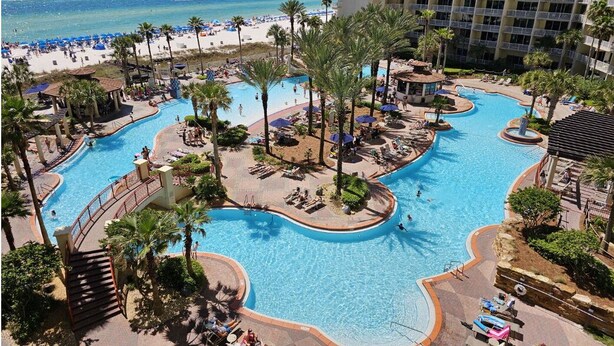 Un resort con varias piscinas, palmeras y vistas a la playa.
