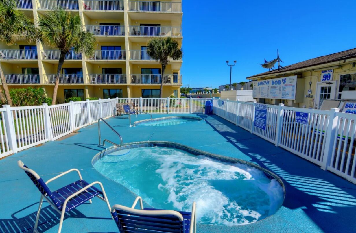 Area piscina di un hotel con idromassaggio, sedie a sdraio e una recinzione bianca.
