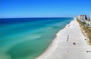 An aerial view of a beach with clear turquoise waters, a sandy shore, and buildings along the coastline. - The Summit 1BR+Bunk/1.5BA -1st Floor! (Panama City Beach)