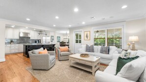 A modern kitchen with white cabinets, a stainless steel range hood, and a black countertop. There is a dining area with a white table and chairs. The living room has a white sofa set and a coffee table. - Private Pool! Serene 4/4 Sleeps 14! (Santa Rosa Beach)