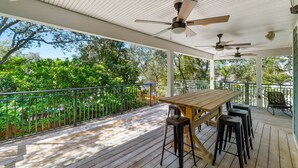 A covered outdoor deck with a wooden table and bar stools, surrounded by metal railings and trees. - Private Pool! Serene 4/4 Sleeps 14! (Santa Rosa Beach)