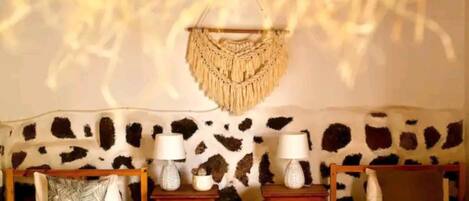 A room with a stone-patterned headboard, two bedside tables with lamps, and a macramé wall hanging.