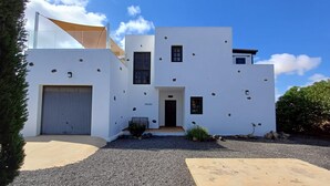 Une maison moderne à deux étages, avec une façade blanche, un garage et une allée gravillonnée.