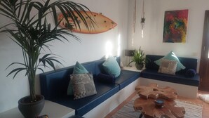 Un salon moderne avec un canapé bleu, une grande plante en pot, une décoration sur le thème du surf et un tableau abstrait aux couleurs vives.