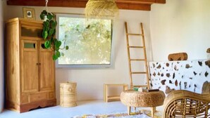 Une pièce avec un meuble en bois, une chaise en osier, une échelle et une grande fenêtre donnant sur un paysage verdoyant.