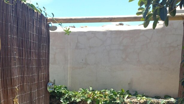 Un baño exterior pequeño con inodoro, pared de piedra y valla de bambú.