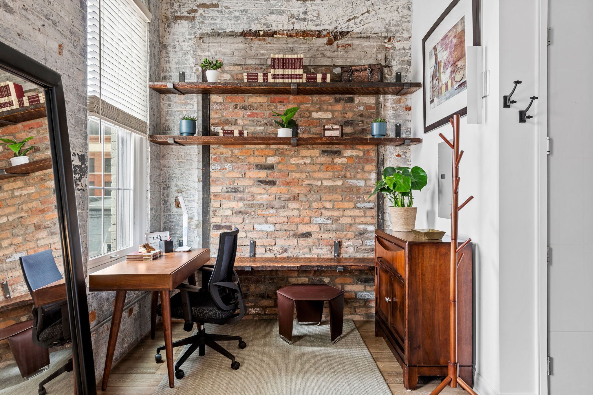 A rustic office space with exposed brick walls, wooden shelves, and a desk with office chair.