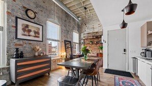 A modern kitchen with a rustic brick wall, a dining area with a wooden table and chairs, and a large window providing natural light.