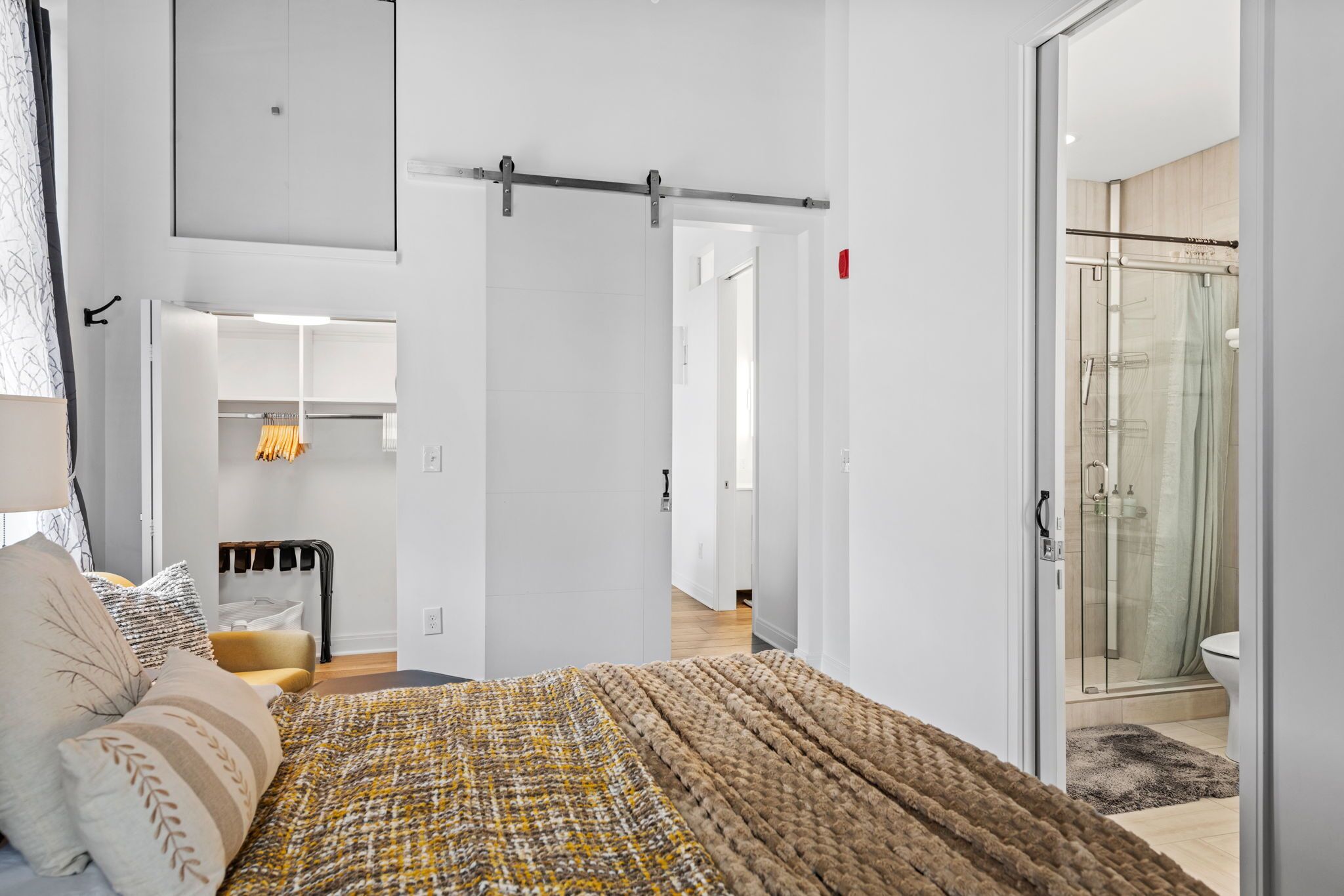A modern bedroom with a bed, a wardrobe, and a bathroom with a glass shower.