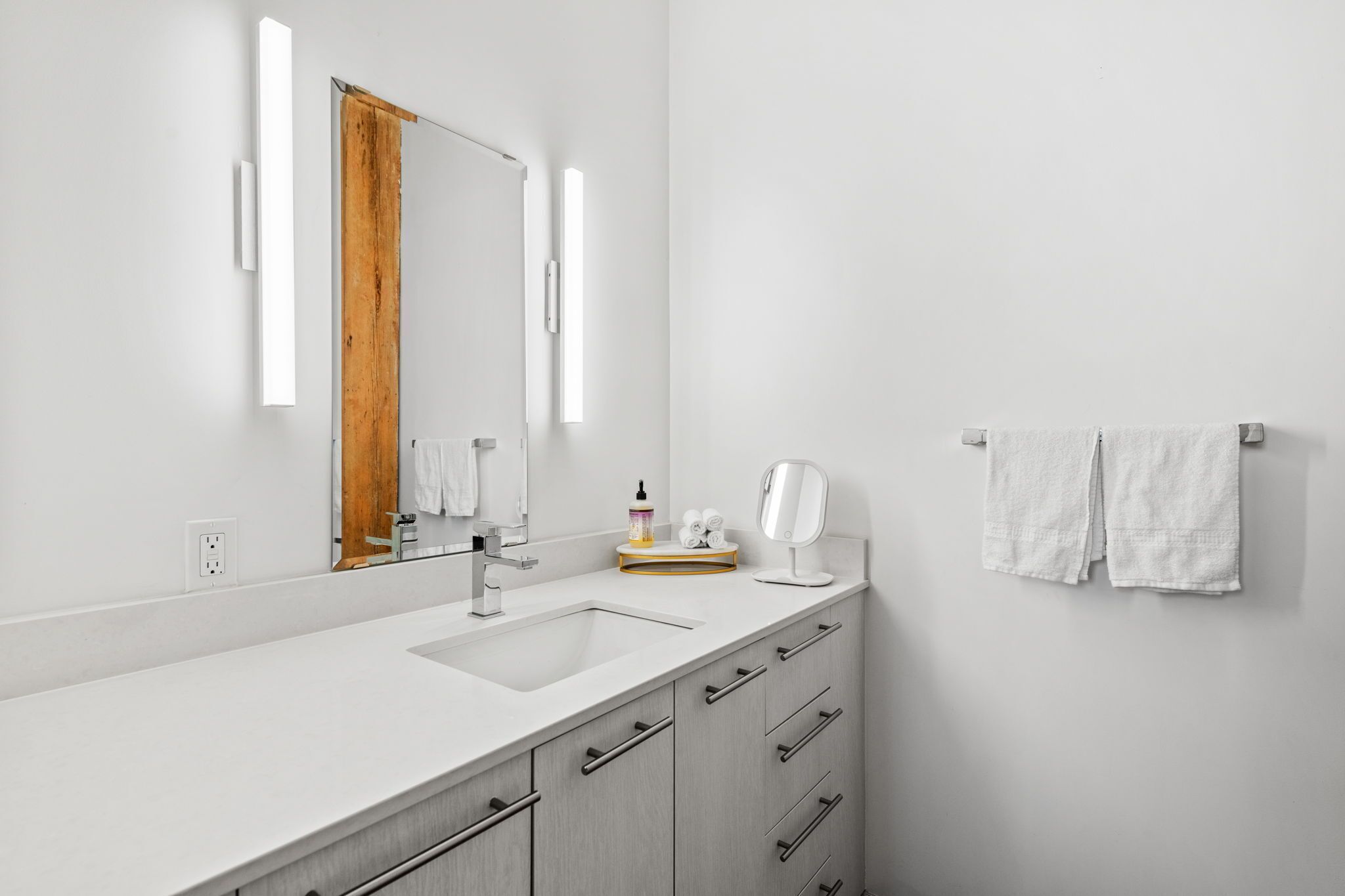 A modern bathroom with a white sink, a mirror, and a towel rack.