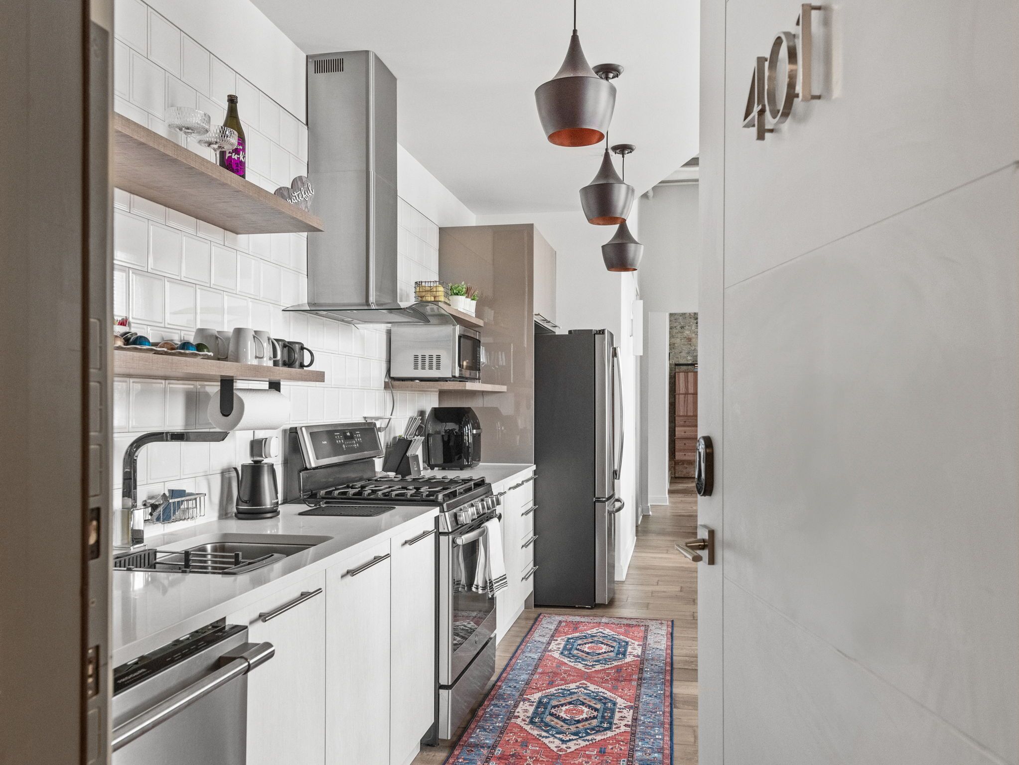 A modern kitchen with white cabinetry, stainless steel appliances, and a patterned rug.