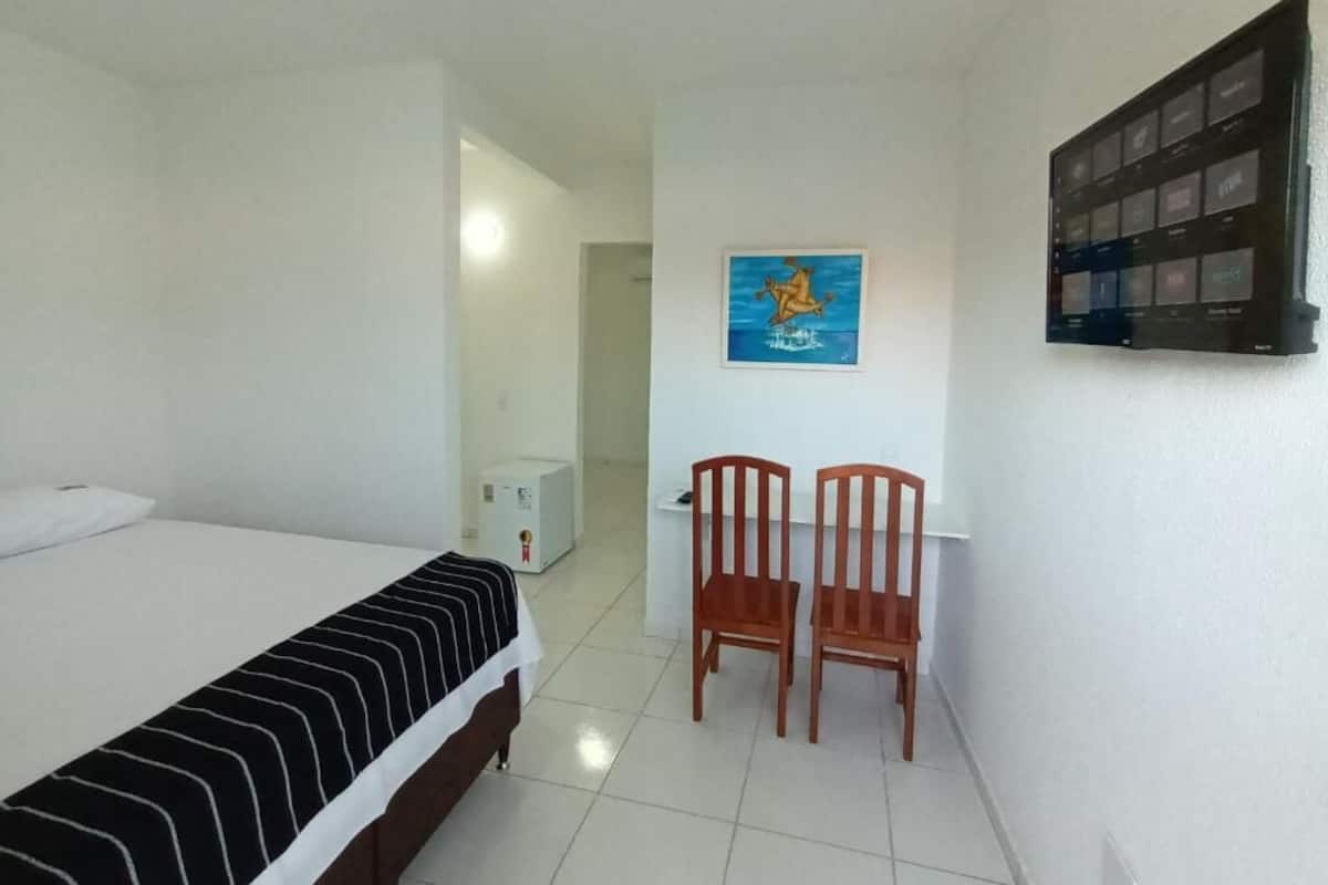 Une chambre d’hôtel avec un lit, deux chaises en bois, un bureau et un téléviseur fixé au mur.