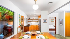 Een moderne keuken met houten kastjes, een eethoek met een houten tafel gedekt voor vier personen, en uitzicht op een balkon met groen.