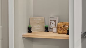 A hallway with a shelf displaying a welcome sign, a Matisse painting, and a woven basket. - Cozy Queen Bed + Sofa Bed Studio | Free Parking | Mins to DT | VAMC | UTHSC (Memphis)