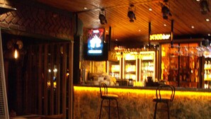 Un área de bar con un televisor montado en la pared, techo de madera y taburetes de bar.