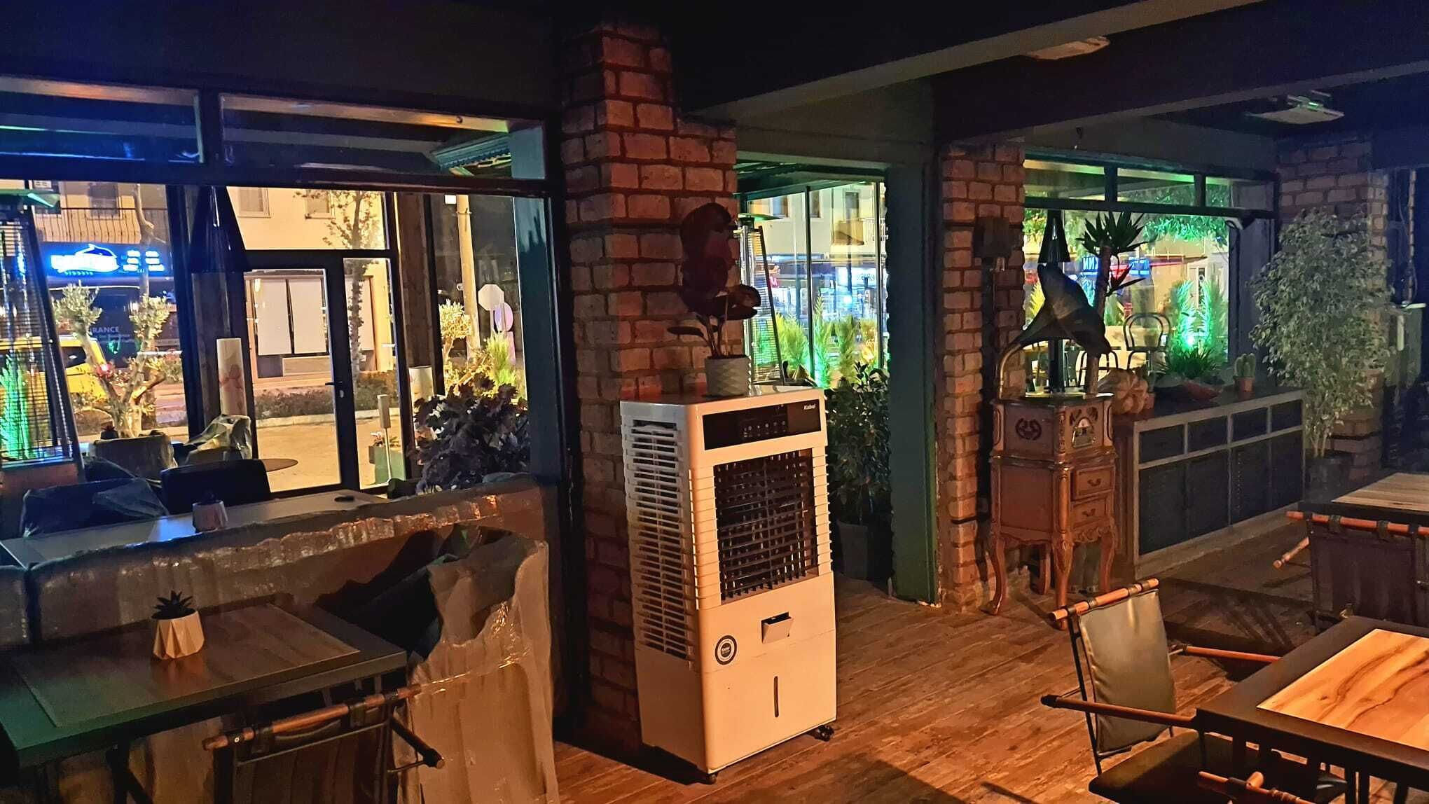A cozy restaurant interior with brick walls, a large air conditioning unit, and a view of the street outside.