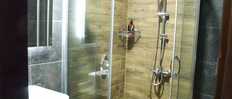 A modern bathroom with a glass-enclosed shower, a white sink, and a small shelf with toiletries.