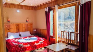 A wooden room with a bed, a table, and a window with curtains. - Tirthan Riverside Cottage (Banjar)