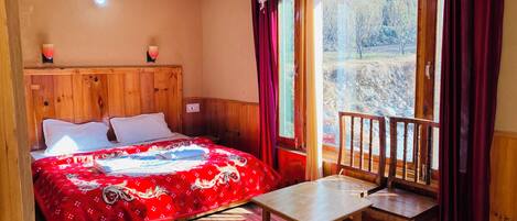 A wooden room with a bed, a table, and a window with curtains.